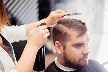 Hairdresser woman doing hairstyle to bearded man in barbershop