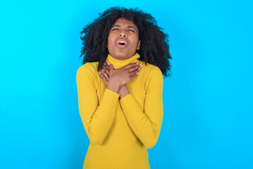 Young woman with afro hairstyle wearing yellow turtleneck over blue background shouting suffocate...