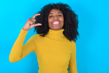 Young woman with afro hairstyle wearing yellow turtleneck over blue background smiling and...