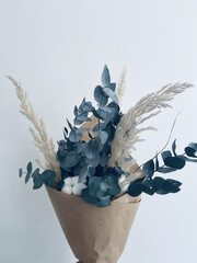 Vertical shot of aesthetic bouquet with blue artificial leaves and pampas against a white background