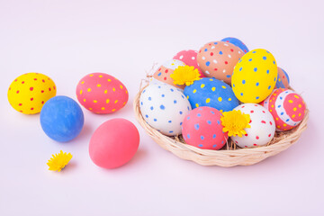 Colorful eggs in a basket with yellow Chrysanthemum flowers on pink background