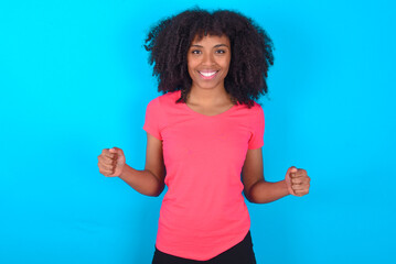 Happy Young girl with afro hairstyle wearing pink t-shirt over blue background Holding Empty Paper Board Advertising Offer Text Standing. Autumn Advertisement Banner.