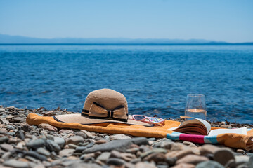 Holiday concept photo of a yellow towel with brown sun hat book and a glass of water at the seaside beach