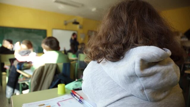 Back view of an unrecognizable young girl student participating in a class at school, unrecognizable teacher explaining the lesson.
