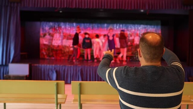 unrecognizable drama teacher directing a group of unrecognizable boys and girls in a play in the school theater.
