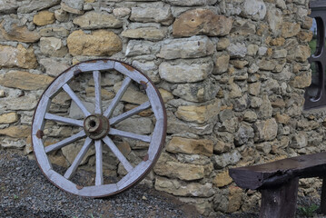 An outdated old wooden wheel from a horse-drawn cart near the stone wall of an ancient house. Detail of a wooden old carriage. Rural retro still life. Decorations in the yard. Place for text. Ukraine.