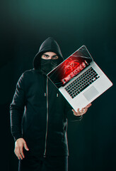 You could be next. Portrait of a computer hacker balancing a laptop while standing against a dark...