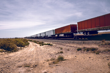 Beautiful shot of a goods train on the desert with blue cloudy sky on a sunny day - obrazy, fototapety, plakaty