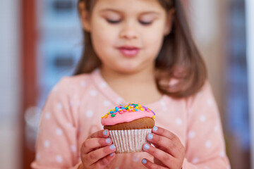 Take a look at my delicious dessert. Cropped shot of a little girl looking at a cupcake in her hands.