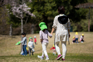 Obraz na płótnie Canvas 桜満開の公園で遊んでいる保育園の子供達と先生の姿
