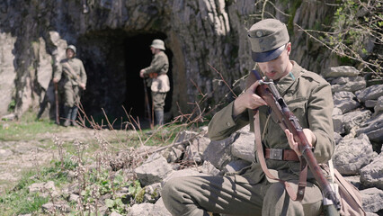 Austro-Hungarian soldier check the rifle while sitting on rock by military cavern