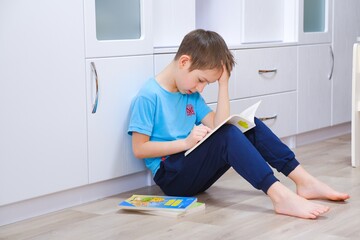 Boy of primary school age teaches lessons and reads a book sitting on the floor. Crafting....
