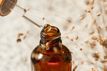 Pipette close-up with serum or oil and an amber bottle. Skincare products, natural cosmetic. Beige...