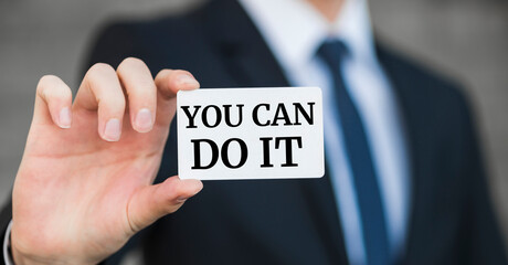 Man holding white card with quotes YOU CAN DO IT on wall background