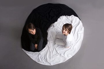 Two children, dressed in black and white, lying on the floor in Yin -Yang circle - obrazy, fototapety, plakaty