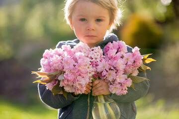 Sweet blond boy, holding pink flowers in garden