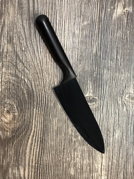 The black knife lying on the table with wooden texture.