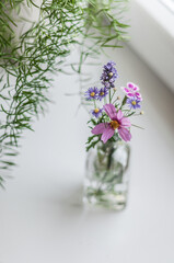 A small bouquet of wildflowers in a glass vase on a windowsill next to an asparagus top view.