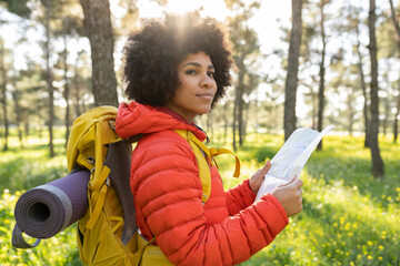 Attractive afro american woman hiker with backpack hiking in the forest at sunset while holding a...