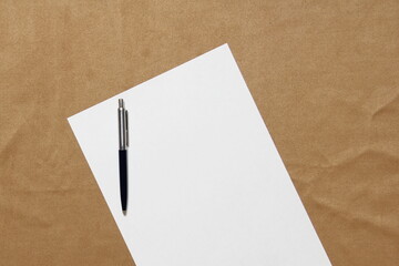 Template of white paper with pen lies diagonally on light brown cloth background. Concept of business plan and strategy. Stock photo with empty space for text and design.