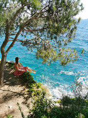 Obraz premium Girl tourist sits in a pine forest on the rocks on a background of beautiful seascape. Mediterranean Sea in Turkey, Kusadasi. Summer background.