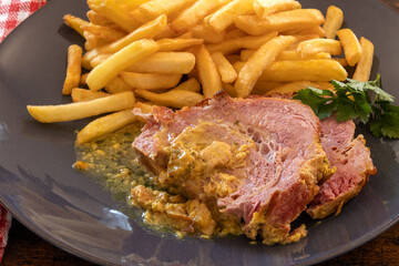 close up of a slice of roast pork with mustard on a plate with french fries