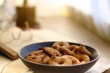 Plate of chocolate chip cookies and sugar cookies, vintage books and reading glasses, candle and flower on the table. Hygge at home. Selective focus.