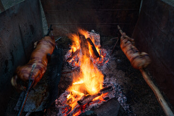 Two whole pigs roasting on a spit next to open flame at evening in long exposure