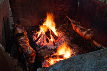 Two whole pig roasting on spit next to fire with sparks in long exposure.