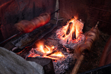 Fototapeta premium Two whole pig roasting on spit next to fire in long exposure