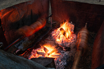 Two whole pig roasting on spit next to fire in long exposure