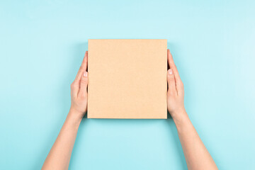 Female hands holding brown ecological package box made of natural corrugated cardboard. Mockup...