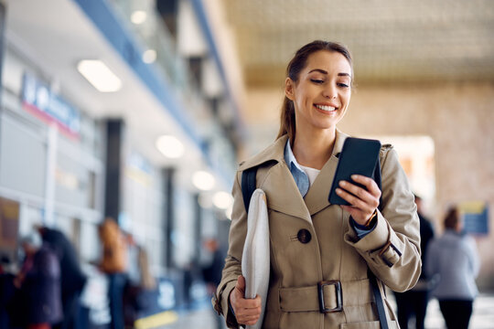 Happy businesswoman uses smart phone at departure terminal at the station.