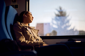 Pensive woman leans on window while traveling by train at sunset.