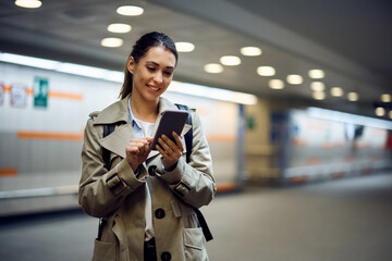 Happy woman uses smart phone while waiting at train station.