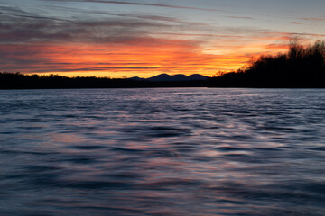Mountain silhouette and colorful clouds reflecting in wavy water at dusk