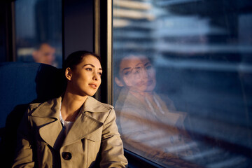 Young woman day dreaming by the window while riding in train at sunset.