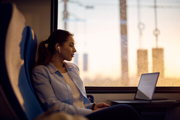 Young woman reads an email on laptop while commuting to work by train.
