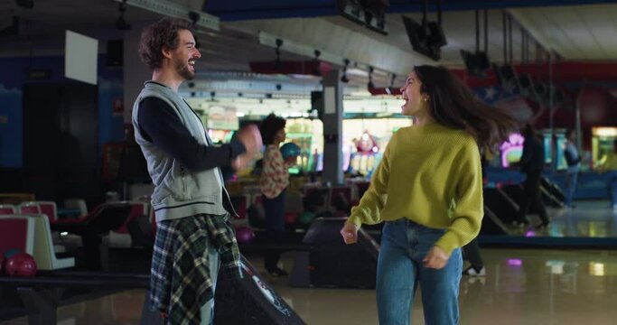 Cinematic shot of happy young multiracial couple in love or college friends having fun to play bowling together in sporting club on weekend.