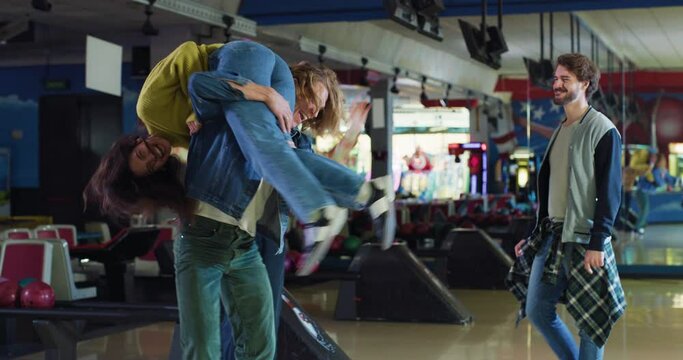 Cinematic shot of happy young arab female bowler throwing strike ball and exulting victory while having fun to play bowling together with multiracial college friends on weekend in sporting club.