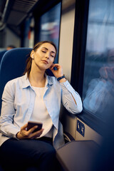 Young woman listens music over earbuds while enjoying train travel with eyes closed.