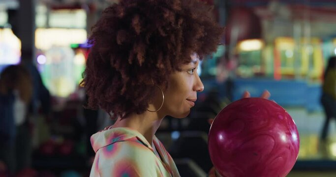 Cinematic close up of concentrated young african black female bowler throwing strike ball and exulting victory while participates in bowling tournament competition in sporting club.