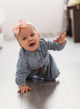 Cute happy 6 months baby girl with pink bow crawling indoor. Pretty smiling kid