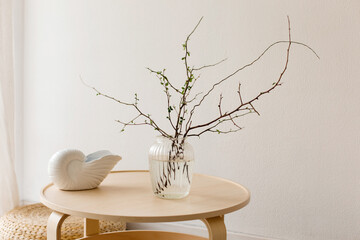 Tree branches in a transparent vase and a ceramic vase on a wooden table against a white wall in...