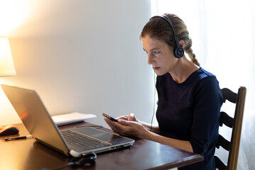 woman sitting at home office desk using headphones and laptop