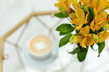 A bouquet of yellow flowers. A glass vase. A cup of coffee. Work.