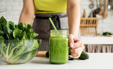 Close up of a young woman holding a jar of green smoothie