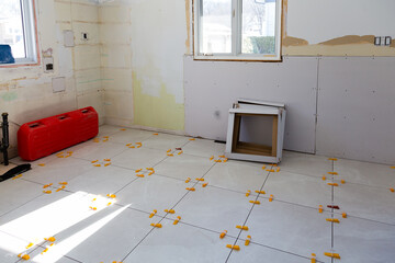 Large square pale ceramic tiles being installed in kitchen in full renovation mode