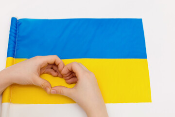 Children against war. Child against background of Ukrainian flag with hands in shape of a heart, painted in yellow and blue.