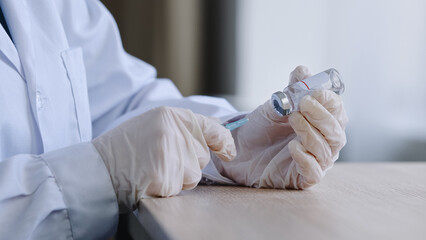 Unrecognizable female doctor pharmacist wearing latex gloves holding syringe and vial bottle of covid 19 liquid vaccine remedy cure drug preparing for injections to immunity and medical treatment